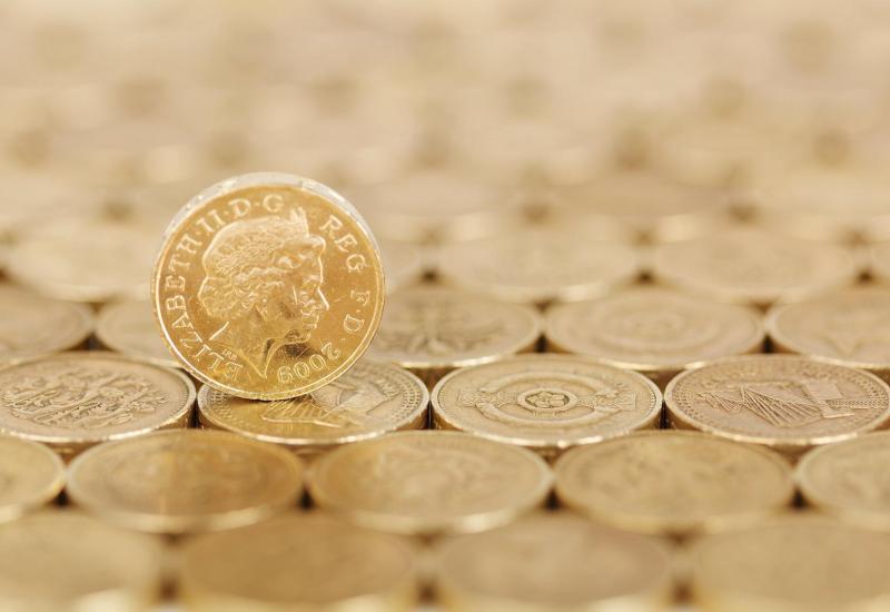 A pound coin sitting on it side on top of other pound coins