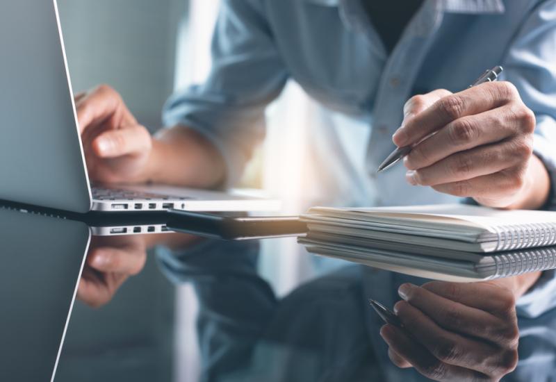 A person working on a laptop and making notes